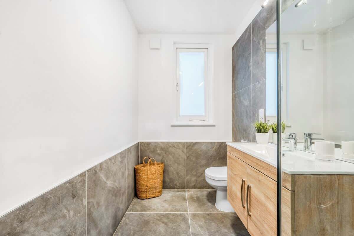 A modern bathroom with a large mirror, a wooden vanity, and a small window.