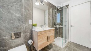 A modern bathroom with a marble floor, a wooden vanity, a glass shower enclosure, and a white door. - DA1 - Modern & Comfy 1-Bed Boutique Apartment (Greater London)