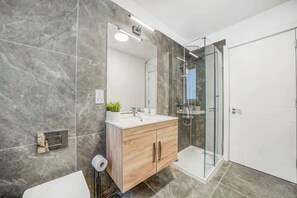 Ein modernes Badezimmer mit Marmorboden, einem Holzbadezimmermöbel, einer Glasdusche und einer weißen Tür.