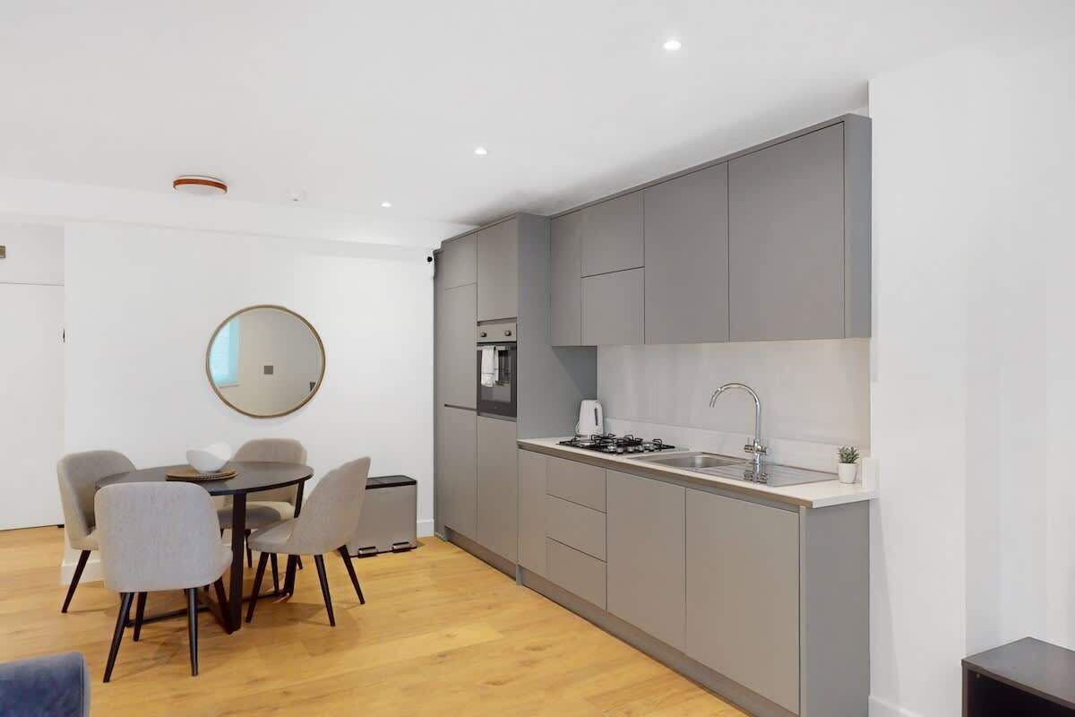 A modern kitchen with grey cabinets, a round mirror, and a dining area with a table and chairs.