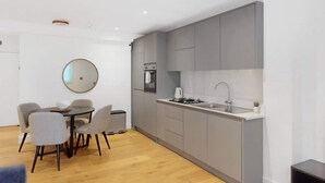 A modern kitchen with grey cabinets, a round mirror, and a dining area with a table and chairs. - DA1 - Modern & Comfy 1-Bed Boutique Apartment (Greater London)
