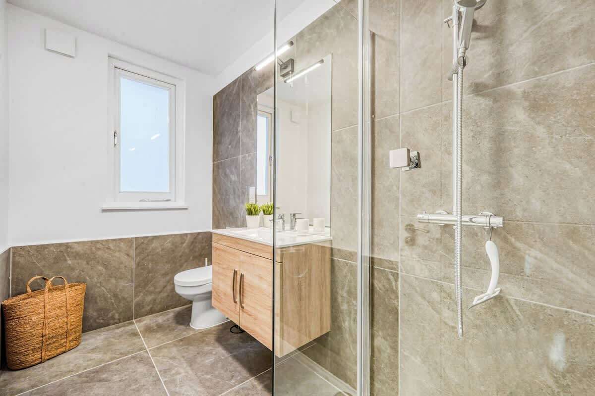 A modern bathroom with a glass shower enclosure, a wooden vanity, and a wicker basket.
