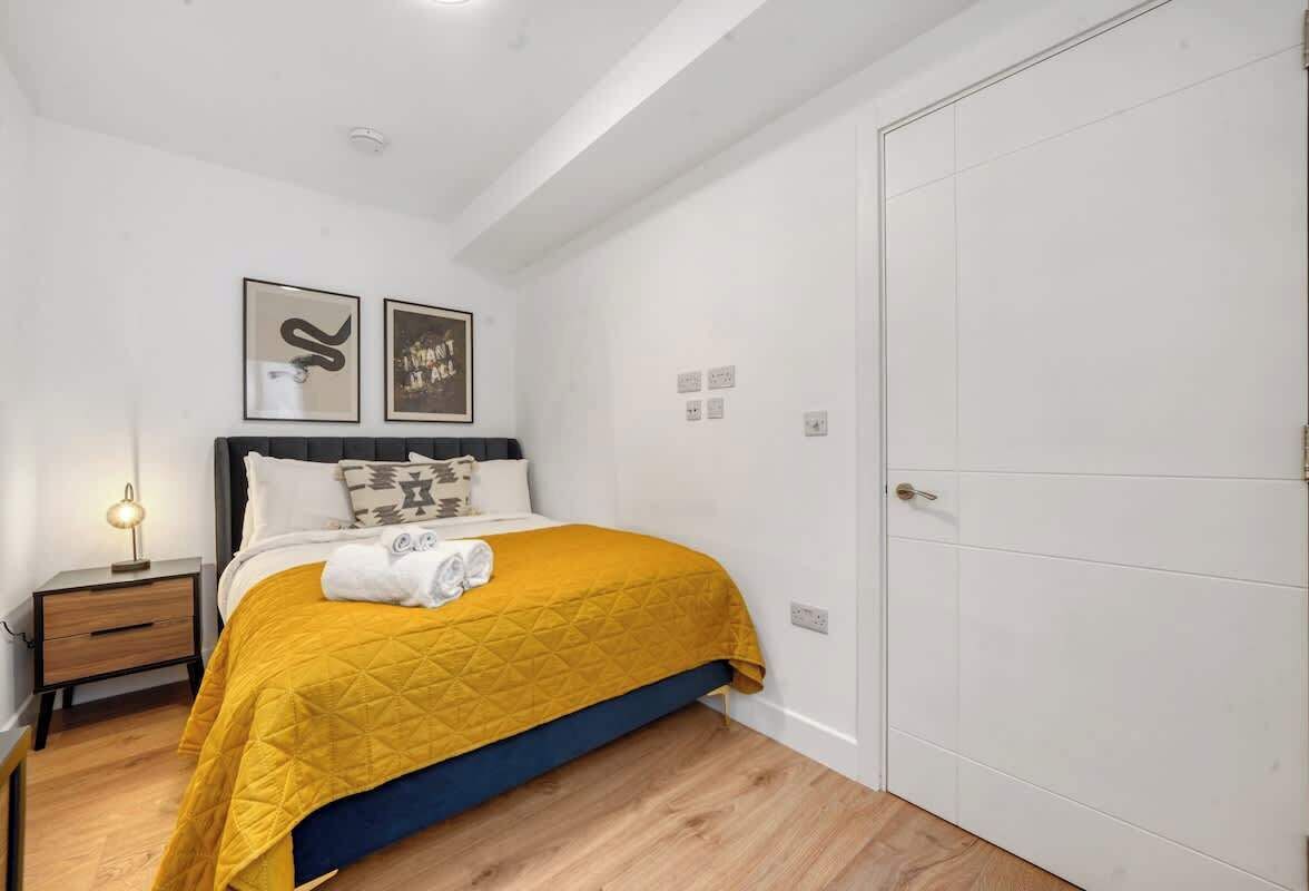 Une chambre à coucher avec un lit, une table de chevet, une lampe fixée au mur et une porte.