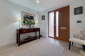 A room with a wooden console table, a vase with flowers, a white chair, and a door. - VW5 - Luxury 3 Bed Townhouse with Parking (Greater London)