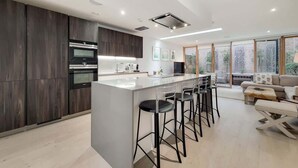Eine moderne Küche mit einer zentralen Kochinsel, Barhocker und einem Essbereich mit einer Couch und einem Tisch.