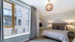 Ein Schlafzimmer mit großem Fenster, einem Bett, Nachttischlampen und einer Deckenleuchte.