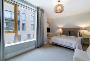 A bedroom with a large window, a bed, bedside lamps, and a ceiling light fixture. - VW5 - Luxury 3 Bed Townhouse with Parking (Greater London)