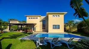 Una casa a due piani con piscina, area salotto esterna e portico coperto.