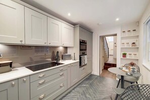 Eine moderne Küche mit grauen Schränken, einem eingebauten Backofen und einem Essbereich mit Tisch und Stühlen.