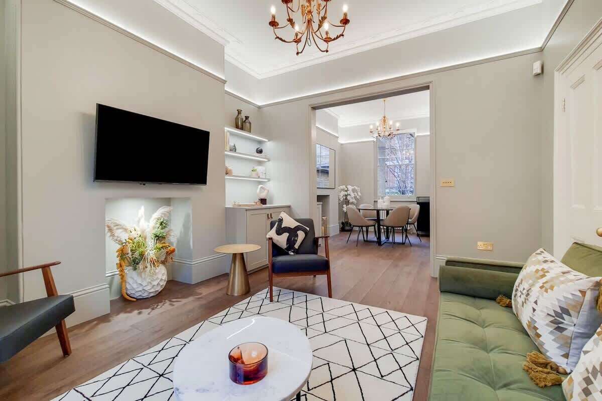 A modern living room with a flat-screen TV, a green sofa, and a dining area in the background.