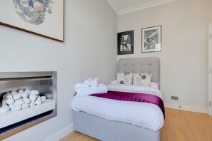 Ein Schlafzimmer mit einem Bett, Kissen, einem Kopfteil, einem an der Wand befestigten Regal mit weißen Gegenständen und zwei gerahmten Bildern.