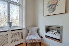 Ein Eckzimmer mit Heizkörper, Stuhl, Kamin und Fenster mit Blick auf Bäume.