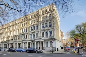 Ein mehrgeschossiges Gebäude im klassischen Stil, mit einer symmetrischen Fassade und gleichmäßig angeordneten Fenstern sowie dekorativen Elementen.