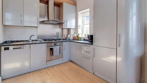 A modern kitchen with white cabinets, a stainless steel range, and a window providing natural light. - CG12 - 2 Bedroom Apt, Kensington Garden Square View (London)