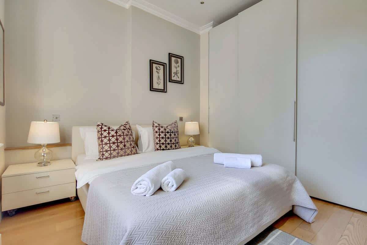 A hotel room with a bed, two bedside lamps, a nightstand, a wall-mounted picture, and a wardrobe.