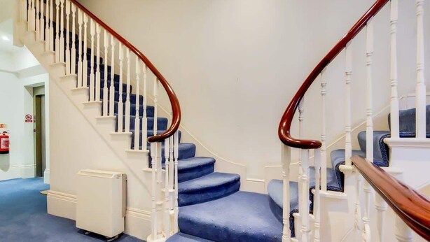 A staircase with white balusters and wooden handrails, leading to a landing with a blue carpeted floor. - CG12 - 2 Bedroom Apt, Kensington Garden Square View (London)