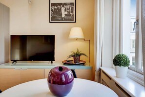 A modern living room with a flat-screen TV, a lamp, a potted plant, and a decorative bowl on a round table. - CG12 - 2 Bedroom Apt, Kensington Garden Square View (London)
