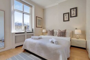 Ein Hotelzimmer mit großem Fenster, einem Bett mit weißer Bettwäsche, einem Nachttisch mit Lampe und einem gerahmten Bild an der Wand.
