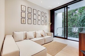 A modern living room with a sectional sofa, a large window with a view of greenery, and framed artwork on the wall. - BR9 - Elegant 2-Bed near Borough Market (Greater London)
