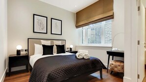 Ein Schlafzimmer mit einem Bett, Nachttischen, einem Schreibtisch, einem Stuhl, einem Fenster und Kunstwerken an der Wand.