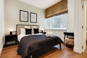Ein Schlafzimmer mit einem Bett, Nachttischen, einem Schreibtisch, einem Stuhl, einem Fenster und Kunstwerken an der Wand.