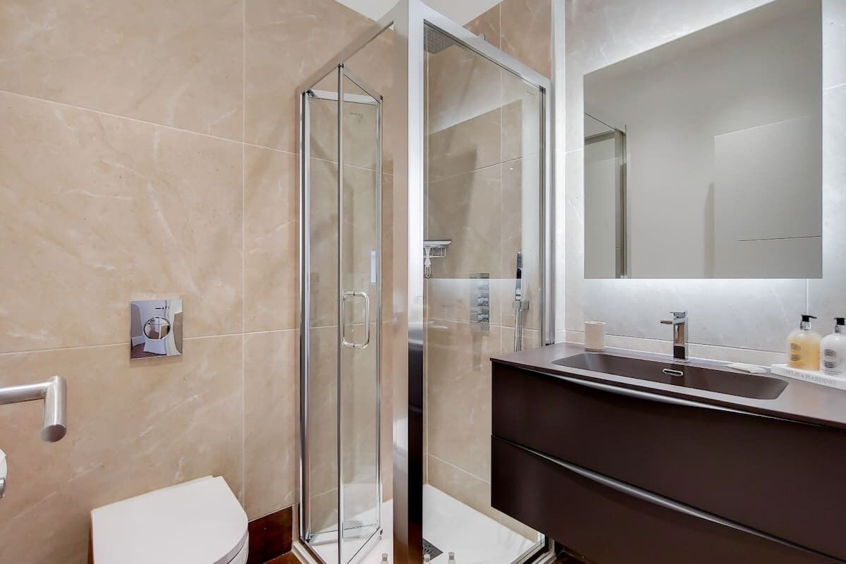 A modern bathroom with a glass shower enclosure, a dark vanity, and a large mirror.