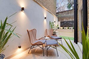 Eine Terrasse mit Korbstühlen und einem Tisch, eine Backsteinmauer und Wandleuchten.