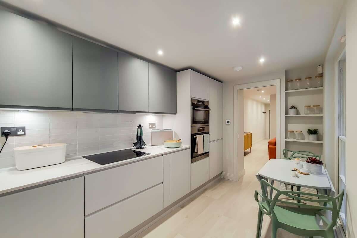A modern kitchen with white cabinets, a black countertop, and a dining area with a white table and green chairs.