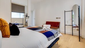 Une chambre d’hôtel moderne avec un grand lit, un fauteuil rouge, un miroir et une petite table.
