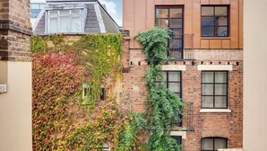 Un bâtiment à la façade en briques, une fenêtre ornée d’un garde-corps en métal et un ciel dégagé.