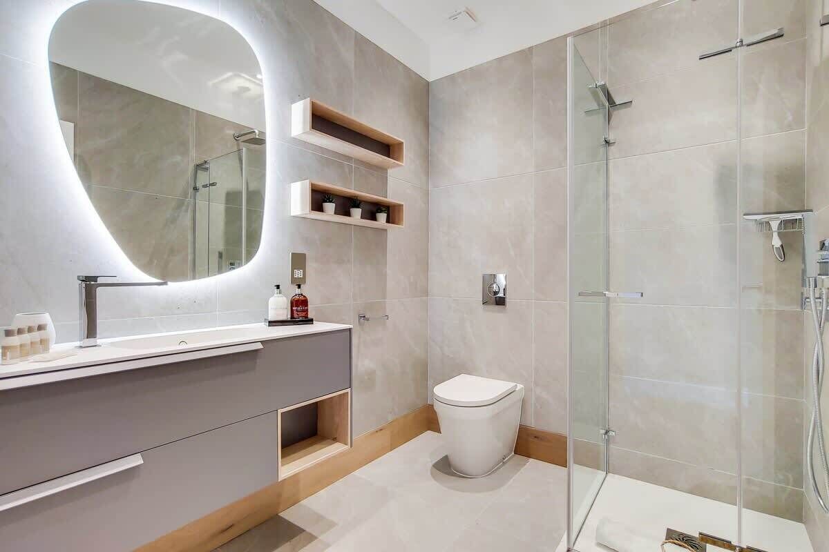 A modern bathroom with a large mirror, a glass shower enclosure, and a toilet.
