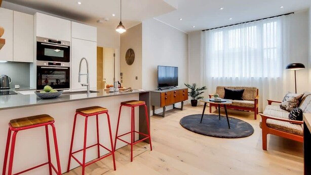 Un appartement moderne comprenant une cuisine, un coin repas et un salon. Il est équipé d’une télévision, d’un canapé et d’une table basse.