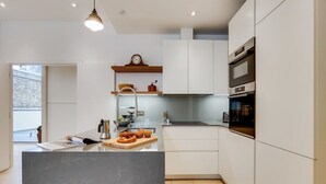 Une cuisine moderne avec des meubles blancs, un îlot central et un four encastré.