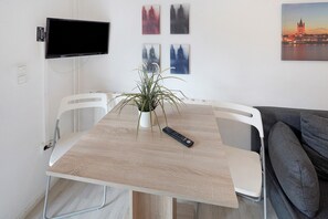 A dining area with a table, chairs, a potted plant, a remote control, and artwork on the wall.