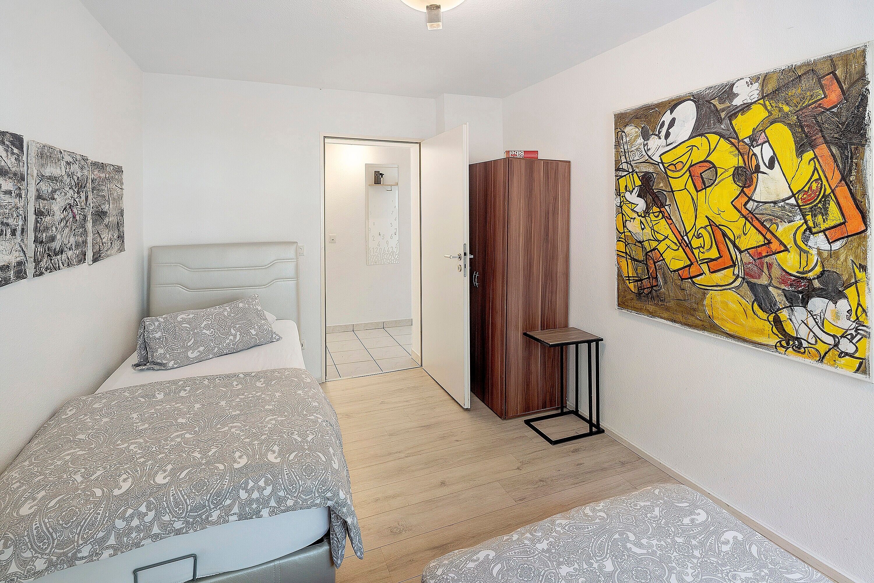 Ein Schlafzimmer mit einem Bett, einem Kleiderschrank, einem Bild und einer Tür zu einem anderen Raum.