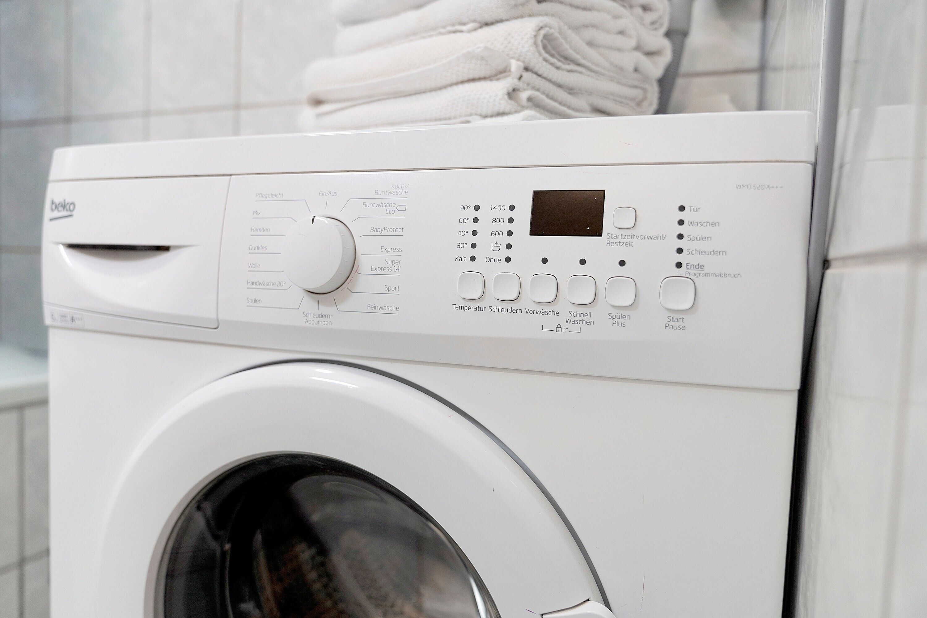 A front view of a white washing machine with control panel, buttons, and a display screen.