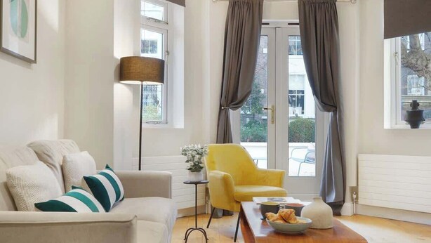 Ein Wohnzimmer mit einer Couch, einem gelben Sessel, einem kleinen Tisch mit Schale und Vase sowie einer Lampe.
