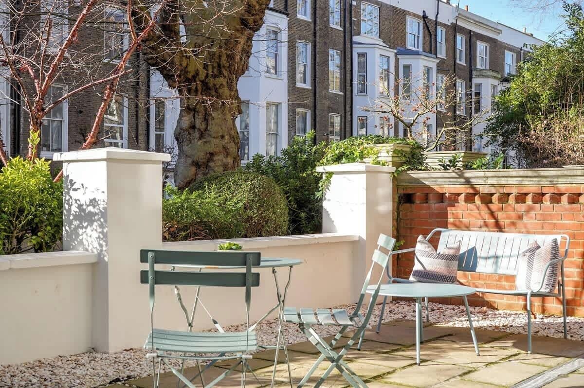 Eine Terrasse mit Tisch und Stühlen, ein großer Baum und eine Ziegelmauer.