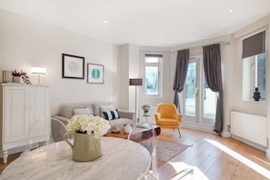 Ein modernes Wohnzimmer mit Sofa, Sessel, Esstisch und Kunstwerken an den Wänden.