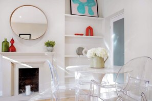 A modern living room with a fireplace, a round mirror, clear plastic chairs, a white table, and decorative items on shelves. - HR2 - Charming 1-Bed near Holland Park (Greater London)