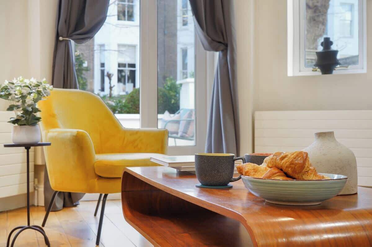 Ein modernes Wohnzimmer mit einem gelben Sessel, einem Holztisch, einer Schüssel Croissants, einer Tasse und einer Vase.