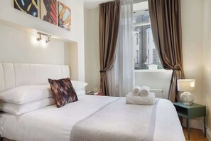 Ein Hotelzimmer mit einem Bett, Kissen, einem Nachttisch, einer Lampe und einem Fenster mit Vorhängen.