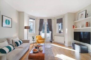 Ein modernes Wohnzimmer mit einer Couch, einem gelben Sessel, einem Couchtisch, einem Flachbildfernseher und einem Bücherregal.