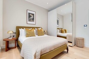 A bedroom with a bed, bedside tables, a mirror, and a framed picture on the wall. - BR11 - Contemporary 2-Bed with City Vibes (Greater London)