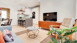 Ett modernt vardagsrum med en soffa, ett soffbord, en tv och en matplats med stolar. I bakgrunden syns ett kök.