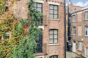 Un edificio de varios pisos de ladrillo con ventanas y un balcón visible, con un callejón estrecho entre los edificios.