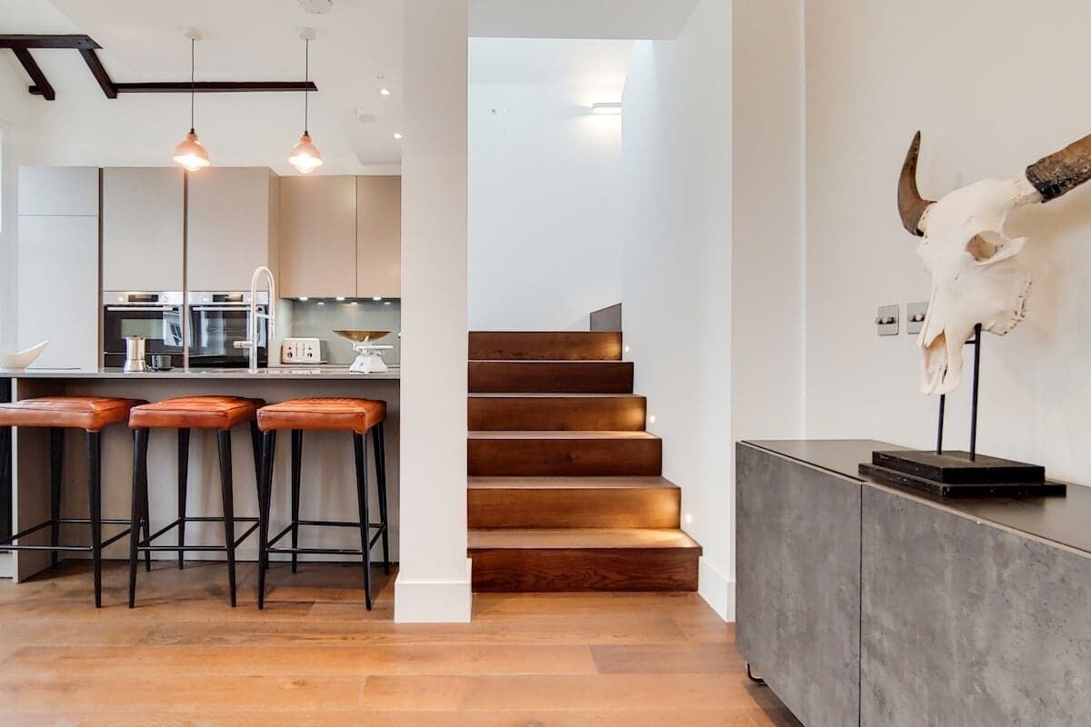 A modern kitchen with bar stools, a staircase, and a bull skull decoration.
