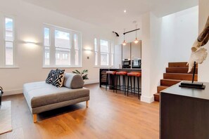 A modern apartment with a sofa, a kitchen area, and a staircase. - BR12 - Modern & Stylish 2-Bed Apartment in Borough (Greater London)