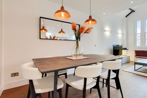 Ein moderner Essbereich mit Holztisch, weißen Stühlen, Pendelleuchten, einer Vase mit Trockenpflanzen und einem großen Spiegel an der Wand.