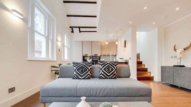 Una sala de estar moderna con un sofá gris, cojines estampados, un jarrón blanco y una planta pequeña sobre una mesita.
